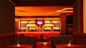 A bar area with a red-lit backdrop, multiple seating arrangements, and a television screen. - Hotel Luciyapalace (Thrissur)