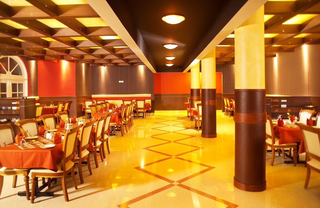 Un vaste espace dédié à la salle à manger, avec de nombreuses tables et chaises, une colonne centrale et un sol orné de motifs géométriques.