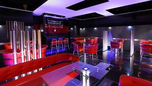 A modern bar area with red bar stools and a glass table, featuring a sleek, contemporary design with reflective surfaces and ambient lighting. - Hotel Luciyapalace (Thrissur)