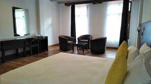 Una habitación de hotel con una cama grande, dos sillones, una mesita, un escritorio y un espejo.