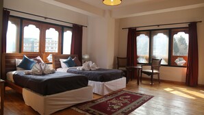 Habitación de hotel con dos camas, piso de madera, lámpara colgante roja y ventanas amplias con cortinas.