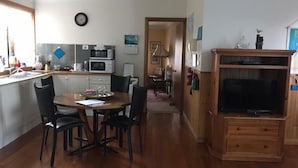 A kitchen with a dining table, chairs, and a TV stand. - Independent holiday unit (Bicheno)