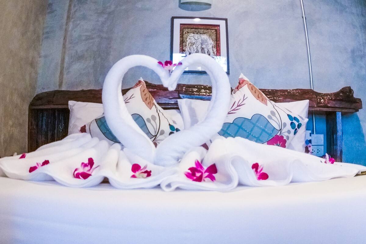 Un lit agrémenté d’une serviette pliée en forme de cœur et d’un coussin décoratif.