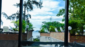A bedroom with a view of a body of water, a brick wall, and some greenery.