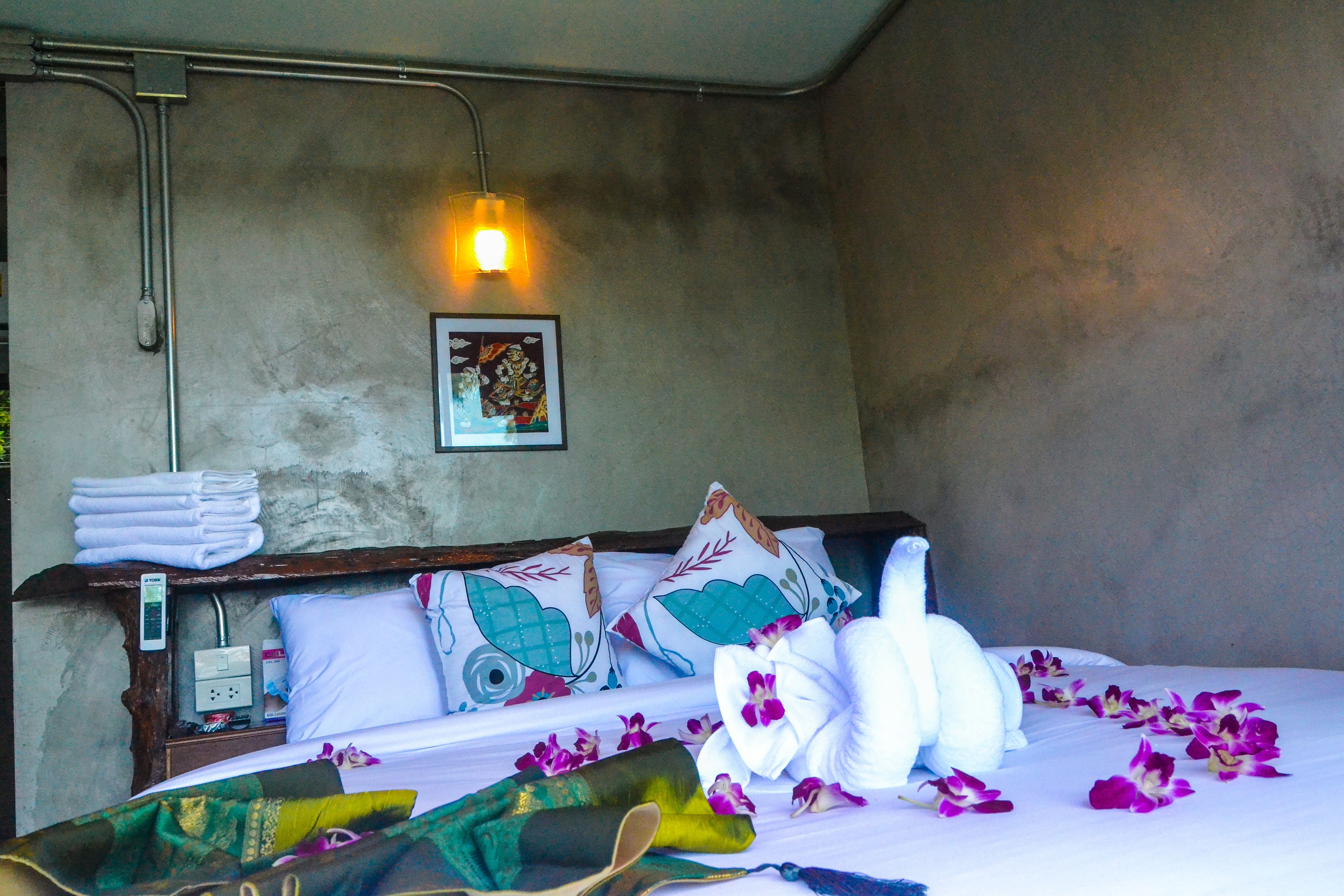 A hotel room with a bed, pillows, a bedside table, a wall-mounted light, and a framed picture.