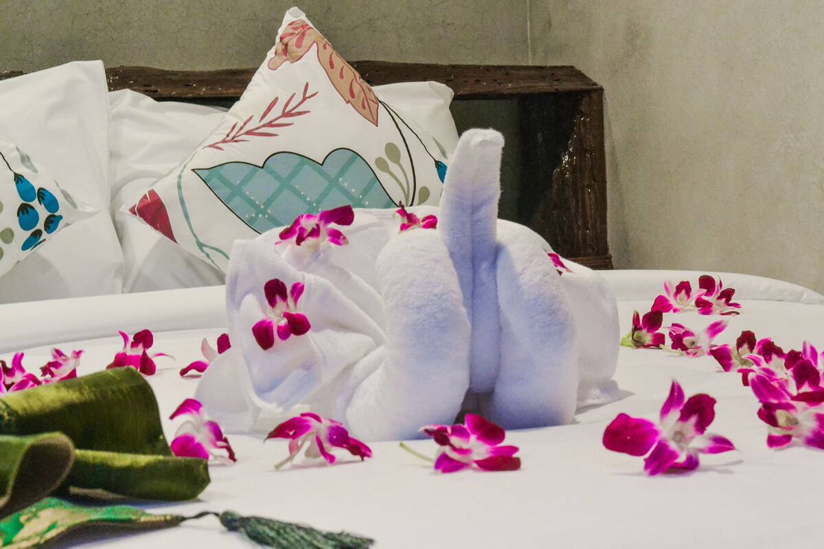 Un lit bien fait, avec du linge de lit blanc et des coussins décoratifs, entouré de fleurs roses et blanches éparpillées.
