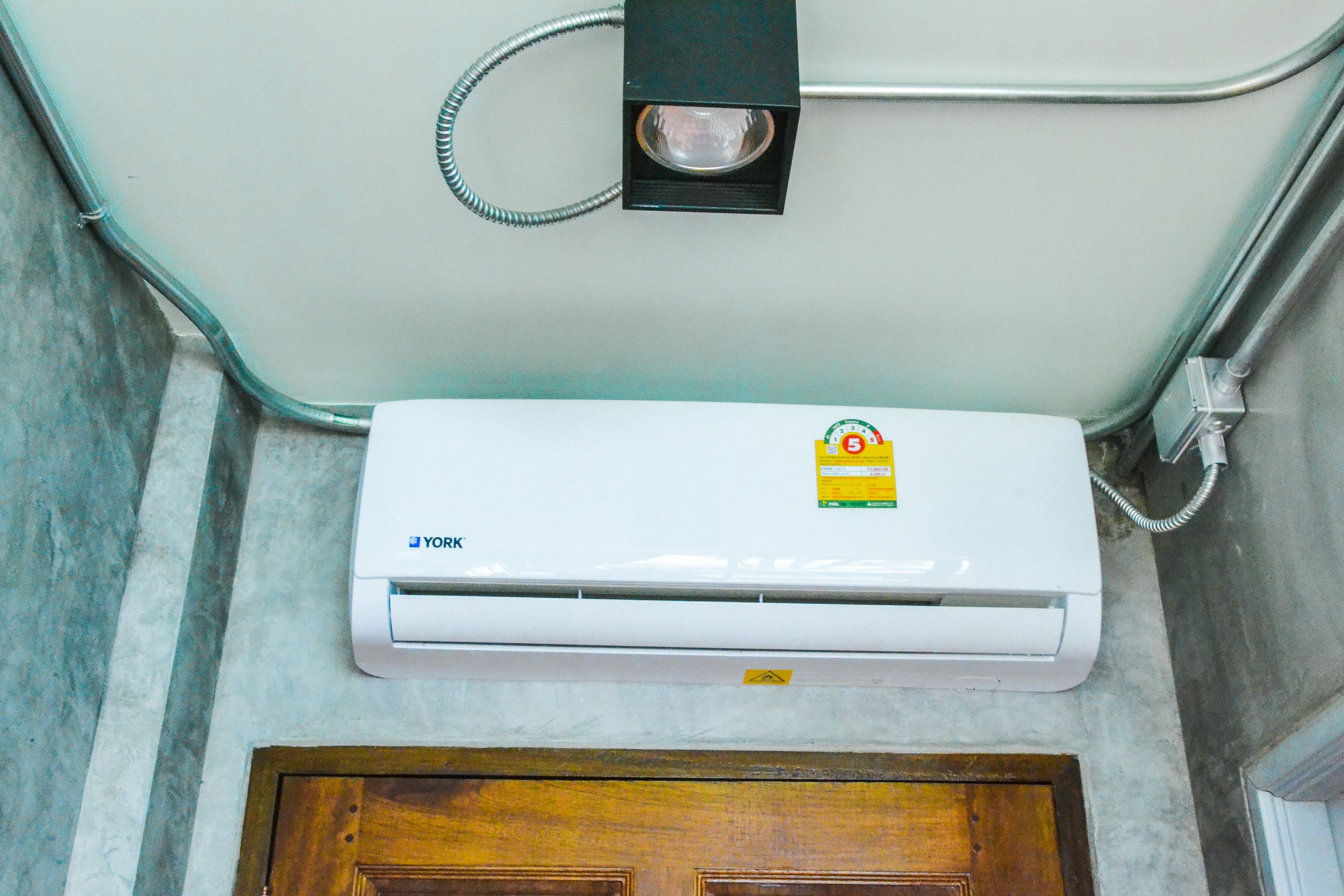 A white air conditioning unit mounted on a wall with a wooden door below.