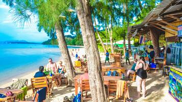 Ein Café direkt am Strand mit Außenbereich, Tischen und Stühlen, mit Blick auf den Strand und das Meer.