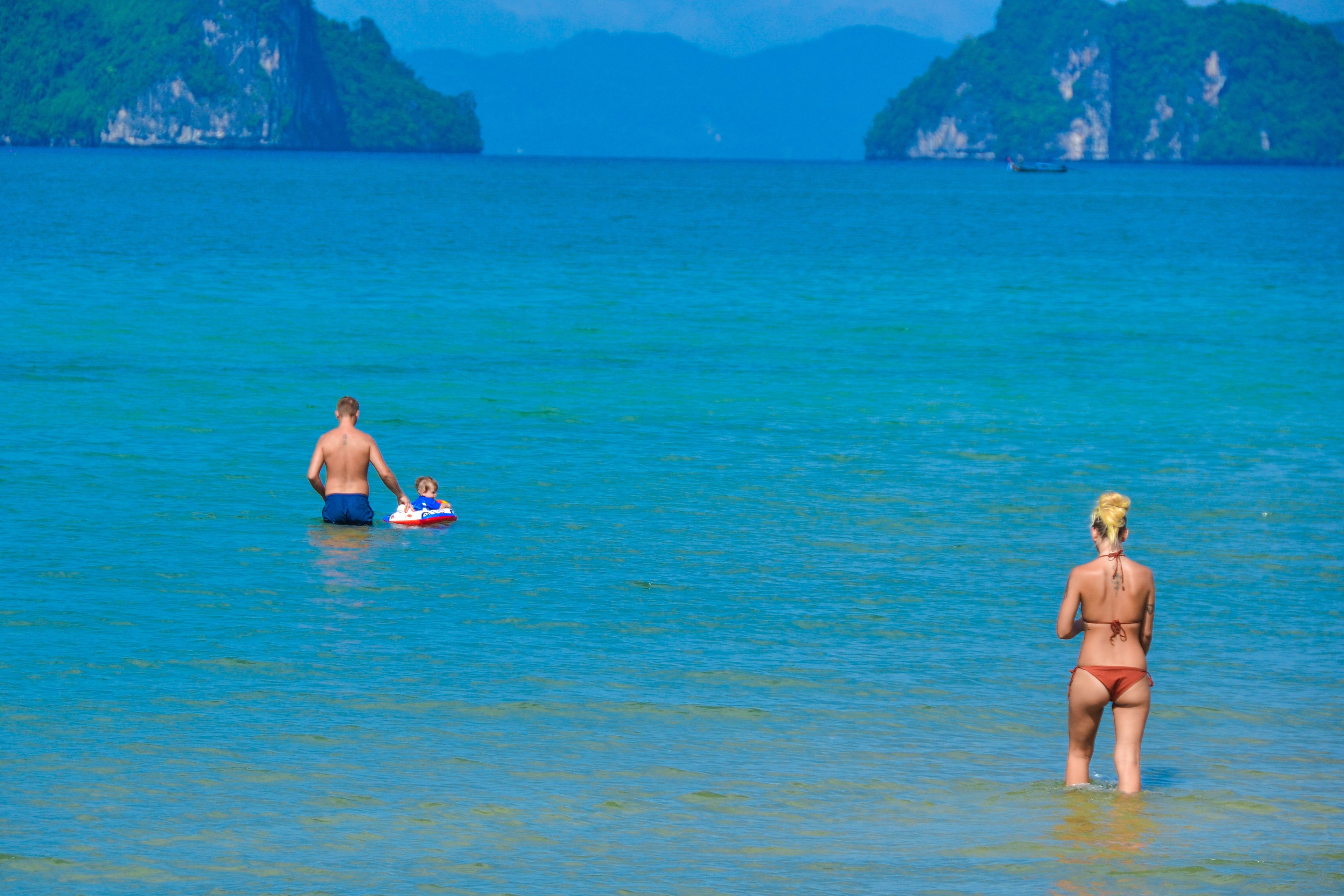 Une scène de plage avec une eau d’un bleu limpide et des collines verdoyantes à l’horizon.