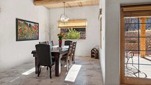 Un espace repas doté d’un plafond en bois, d’une table à manger avec des chaises, d’un lustre, d’une fenêtre donnant sur un paysage verdoyant et d’un tableau encadré au mur.