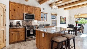 Une cuisine dotée de meubles en bois, d’appareils électroménagers en acier inoxydable, d’un grand îlot central avec des tabourets et d’un coin repas offrant une vue agréable.