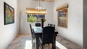 Un espace repas doté d’un plafond en bois, d’un lustre, d’une table avec des chaises et d’une fenêtre donnant sur un paysage verdoyant et un bâtiment.