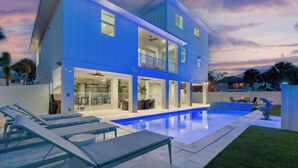 A two-story house with a swimming pool, outdoor seating, and a well-maintained lawn.