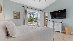 A bedroom with a bed, a TV, a dresser, and a window with curtains. - Sea la Vie offers Bay Views, Pool, and is Pet Friendly (Fort Myers Beach)