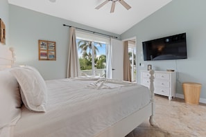A bedroom with a bed, a TV, a dresser, and a window with curtains.