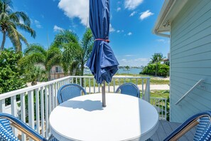 A round table with chairs and a blue umbrella on a balcony overlooking a beach.