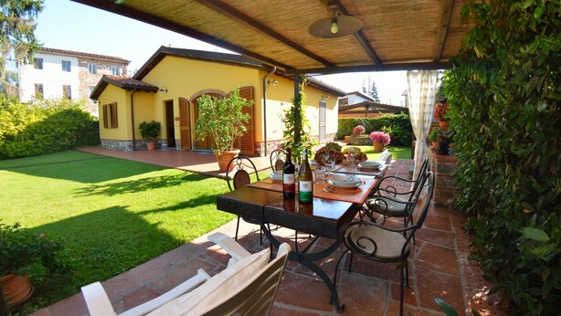 Une terrasse extérieure avec une table dressée pour le repas, entourée de plantes en pot et d’un jardin.