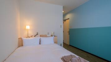 Una habitación de hotel con cama, mesita de noche, lámpara y puerta de baño.