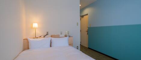 A hotel room with a bed, a nightstand, a lamp, and a bathroom door.