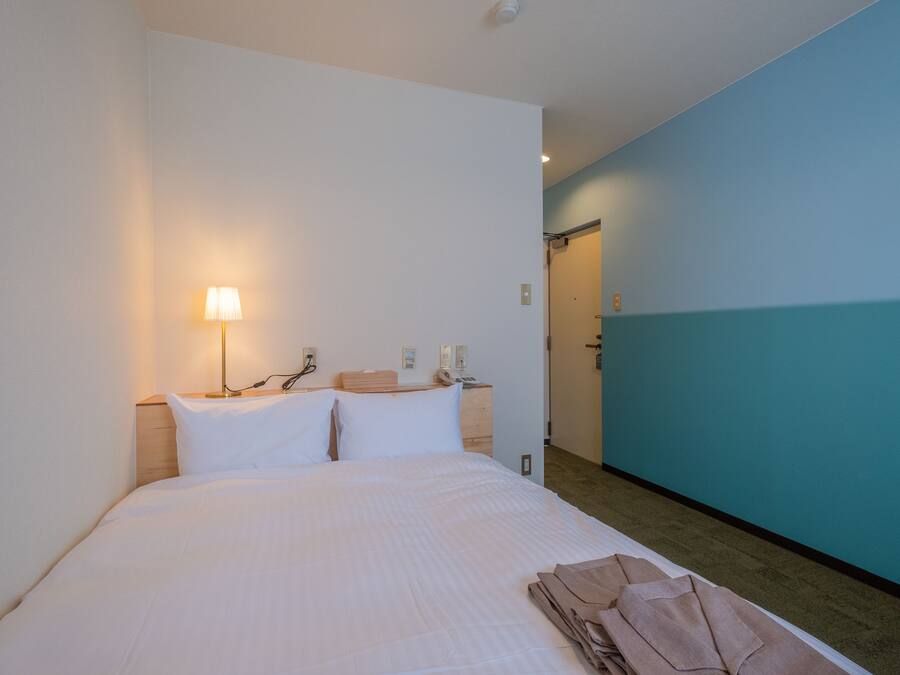 Una habitación de hotel con cama, mesita de noche, lámpara y puerta de baño.