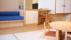 Una habitación pequeña con piso de madera, un sofá azul, una pequeña mesa de comedor con sillas y un armario.