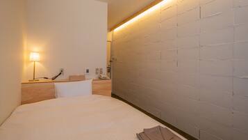 A hotel room with a large bed, a bedside lamp, a wooden headboard, and a brick-patterned wall.