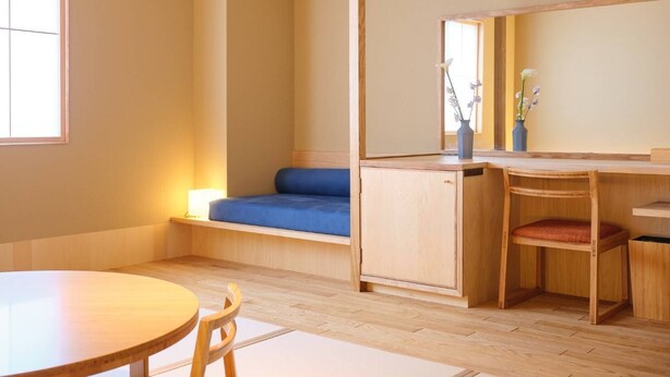 Una habitación con piso de madera, una mesa redonda, un sofá azul y un escritorio de madera con una silla.