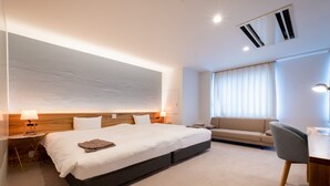 Una habitación de hotel moderna con una cama grande, un escritorio, un sofá y una ventana con cortinas.