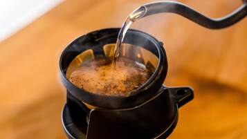 Une cafetière noire avec une anse, remplie d’un liquide sombre, probablement du café, et dont on verse le contenu à partir d’une bouilloire.