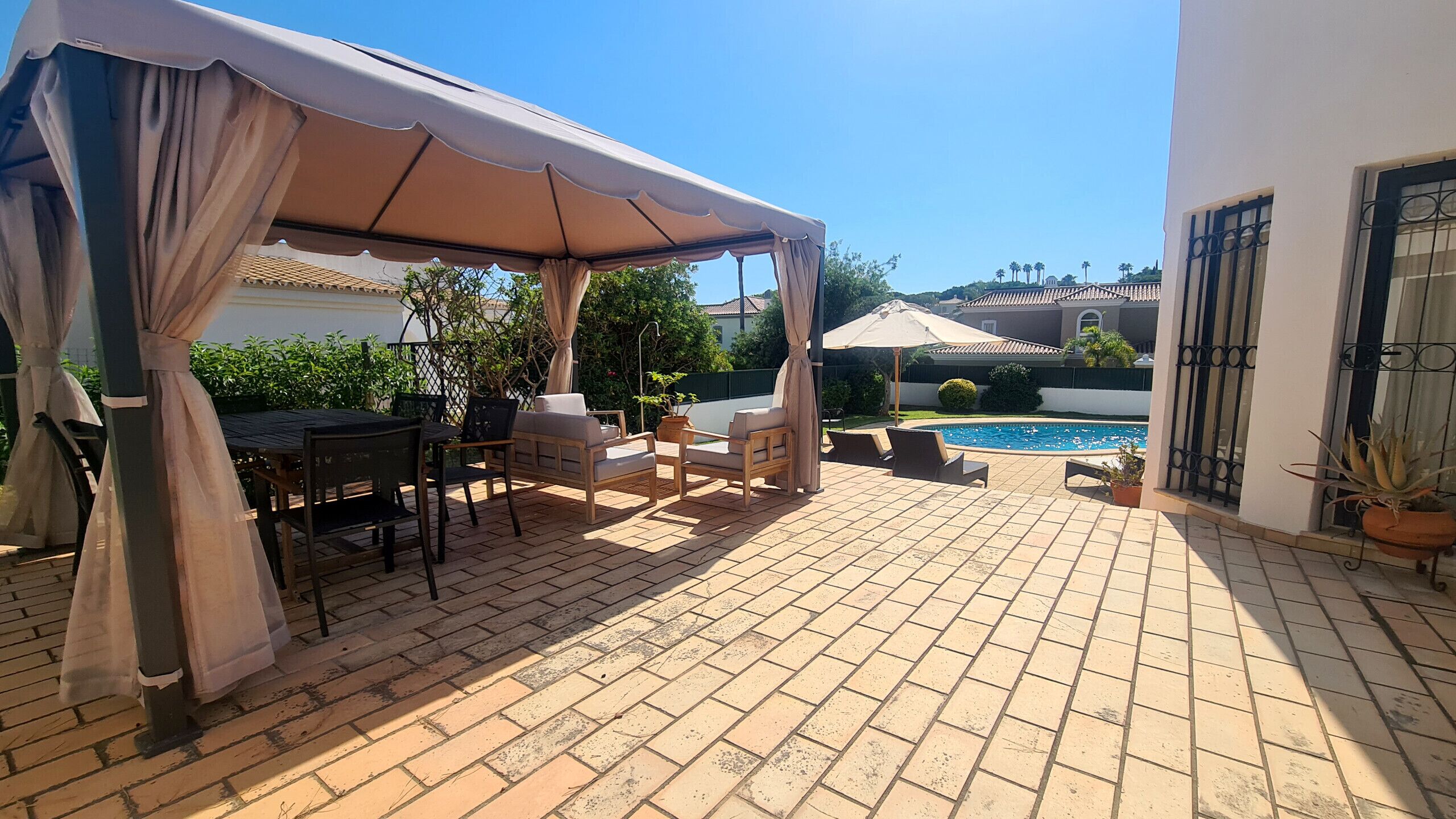 Eine Terrasse mit überdachter Sitzgelegenheit, einem Pool und Blick auf umliegende Gebäude.