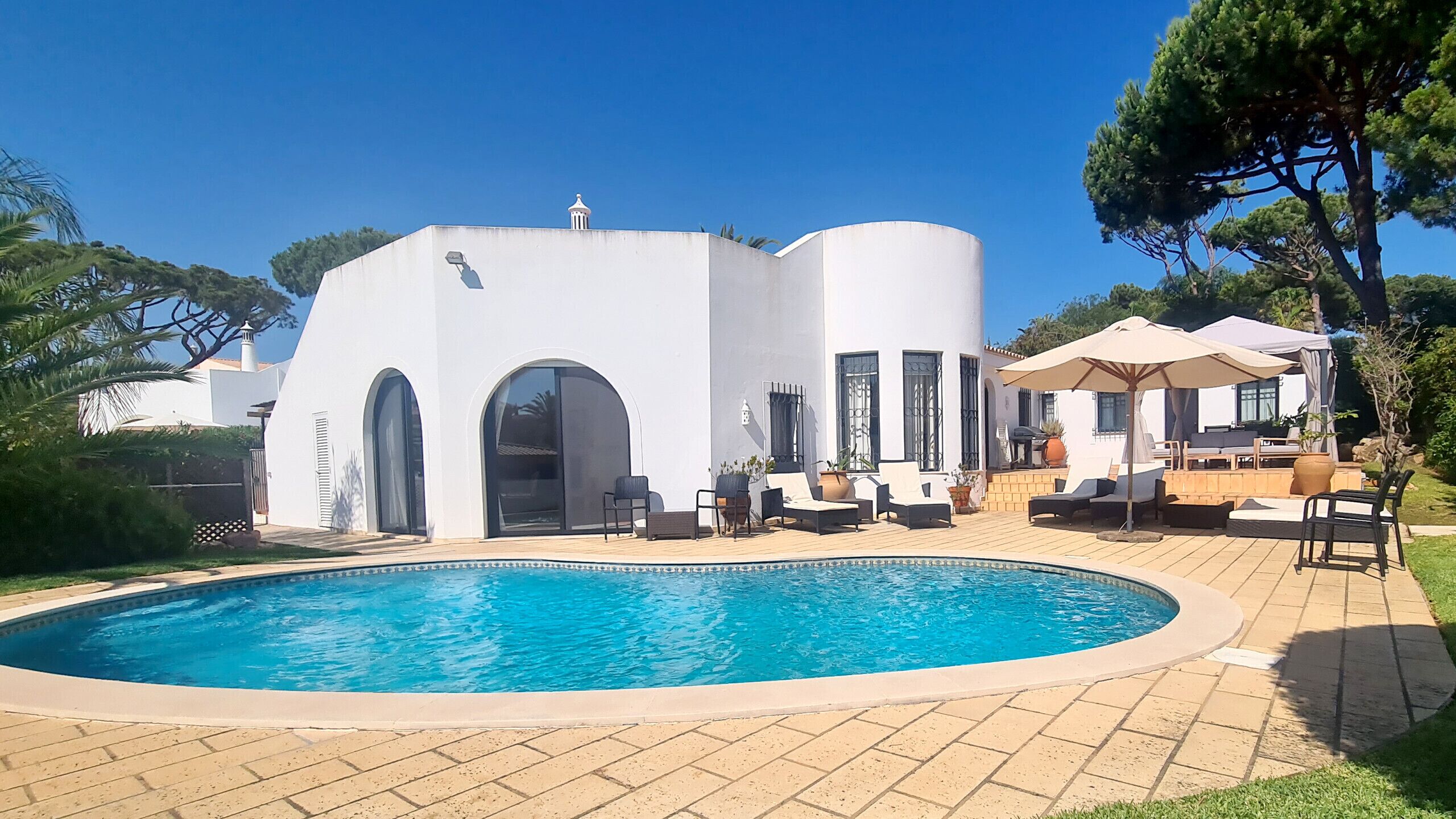 A modern villa with a large pool, outdoor seating, and a white exterior.