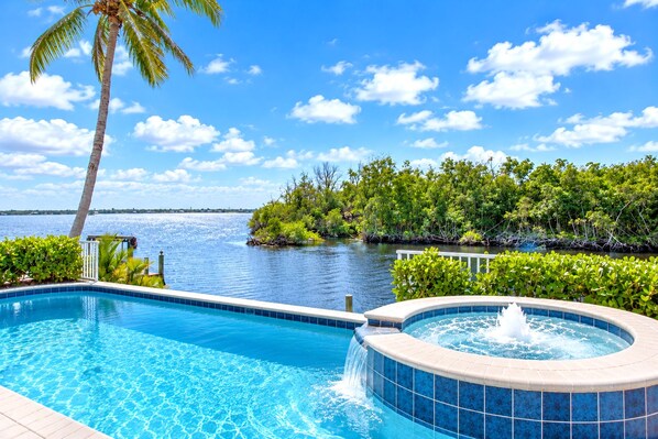 A swimming pool with a hot tub, surrounded by lush greenery and a view of the water.
