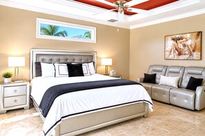 A hotel room with a large bed, a sofa, a ceiling fan, and artwork on the walls.