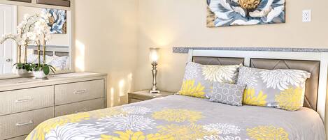 Un dormitorio con cama, mesita de noche, lámpara, cómoda y ventana con plantas.