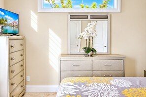 A bedroom with a bed, dresser, vanity, and a TV on a cabinet.