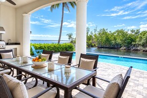 A covered outdoor dining area with a view of a pool and water body.
