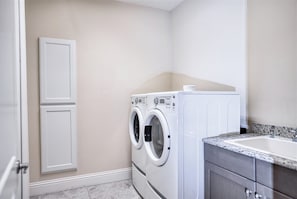 A laundry room with two front-loading washing machines, a small sink, and a cabinet.