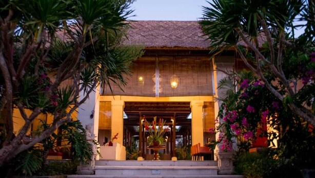 A building with a thatched roof, a staircase leading to the entrance, and a well-maintained garden with tropical plants and flowers. - Villa Pasraman Baghawan (Jimbaran)