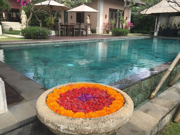 A swimming pool with a flower arrangement in the center, surrounded by outdoor seating and umbrellas. - Villa Pasraman Baghawan (Jimbaran)