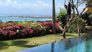 A clear view of an infinity pool with a view of the ocean and a tropical garden with pink flowers. - Villa Pasraman Baghawan (Jimbaran)