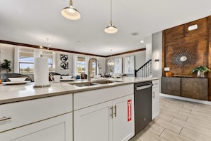A modern kitchen with a large island, pendant lighting, and a wooden accent wall.