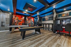 A pool table with a pool cue, a red sofa, and a Star Wars-themed wall.
