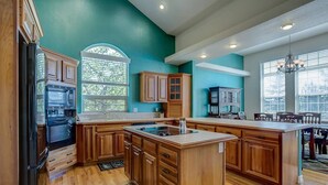 A spacious kitchen with wooden cabinets, a large island, and a view of the outdoors through a window. - Stunning Large Home in Gated Community (Monument)