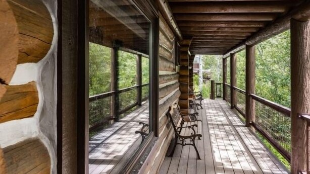 Una terraza cubierta de madera con bancos, ventanas amplias y vistas a la vegetación.