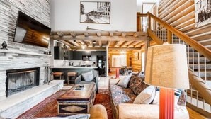 Una sala de estar acogedora con chimenea, un conjunto de sofás, una mesa de centro y una escalera que sube a otro nivel.