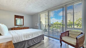 A bedroom with a large bed, a wooden dresser, a chair, and a window with blinds.