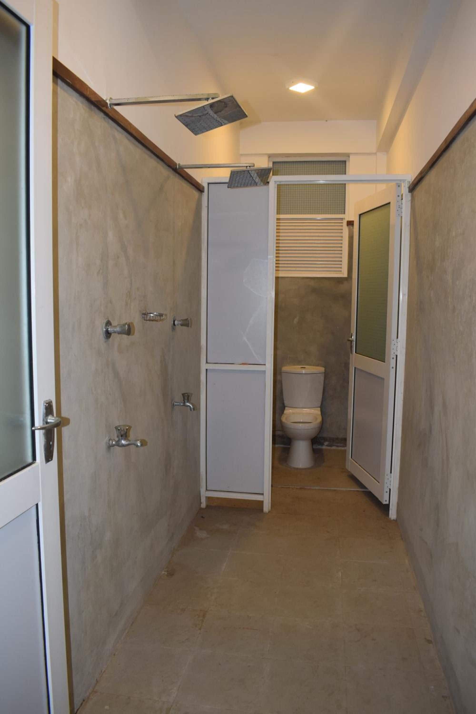 A narrow bathroom with a toilet, a shower stall, and a door leading to another room.