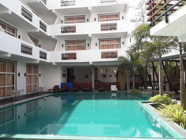 Un hotel de varios niveles con piscina, zona de estar exterior y terraza cubierta.