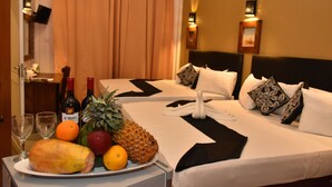 Habitación de hotel con dos camas, una bandeja de frutas en una mesa y dos botellas de vino.