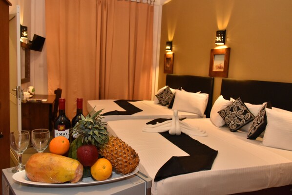 Habitación de hotel con dos camas, una bandeja de frutas en una mesa y dos botellas de vino.